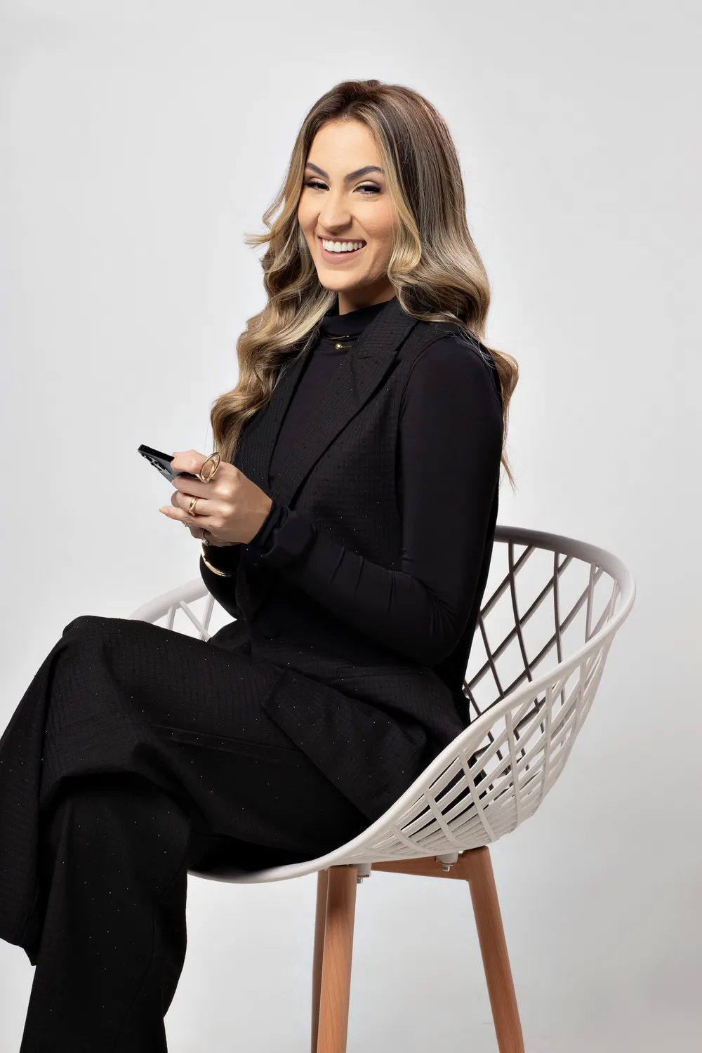 Carol Bessa sentada em uma cadeira, com o celular na mão